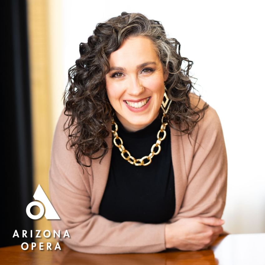 Aurelia Andrews leaning on top of a desk smiling at the camera.